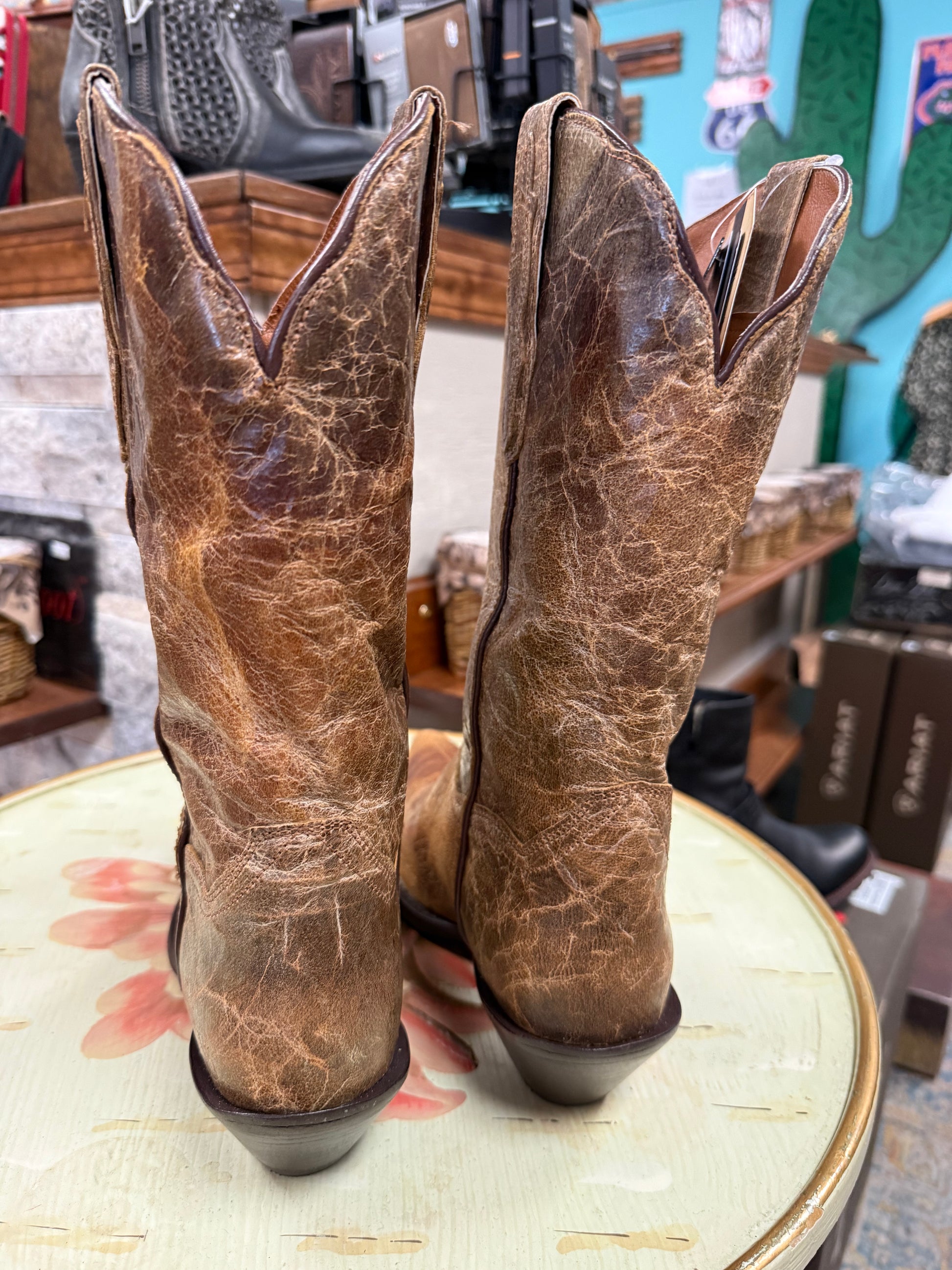 Pair of brown leather cowboy boots on a table with a store setting in the background