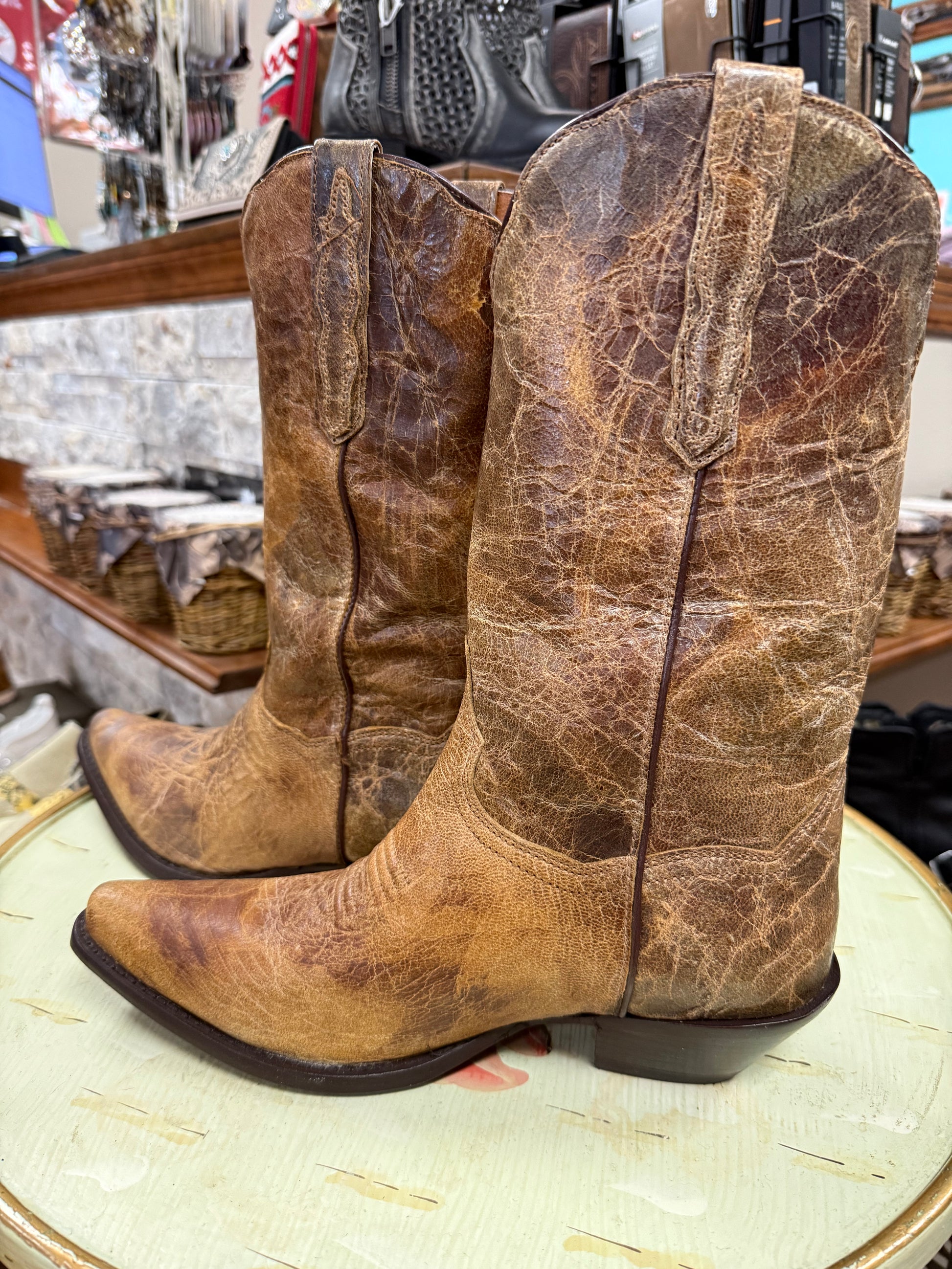 Pair of worn brown cowboy boots on a round surface with a store background.