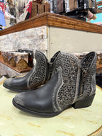 Pair of black ankle boots with decorative patterns on a wooden surface.
