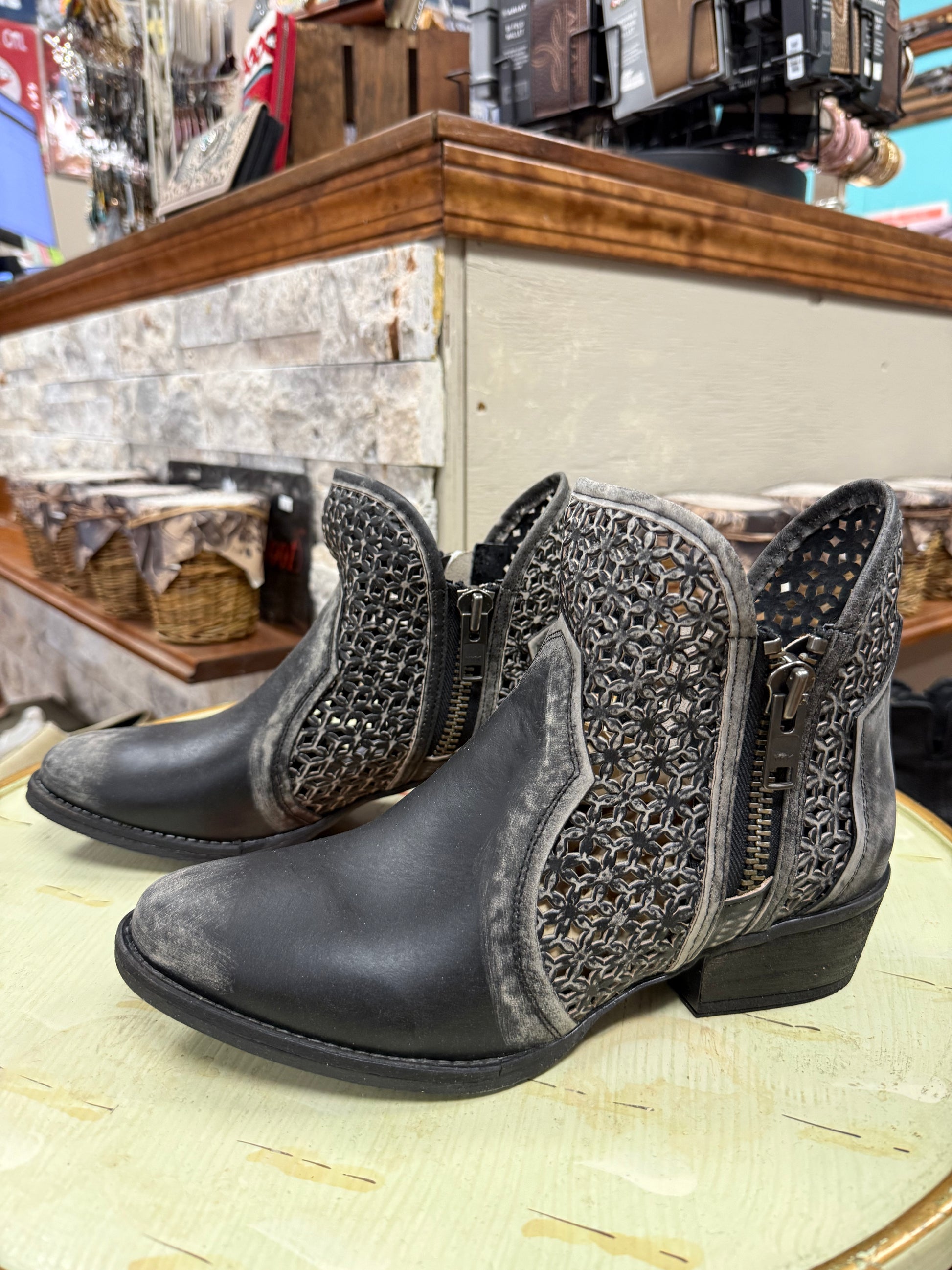 Pair of black ankle boots with decorative patterns on a wooden surface.