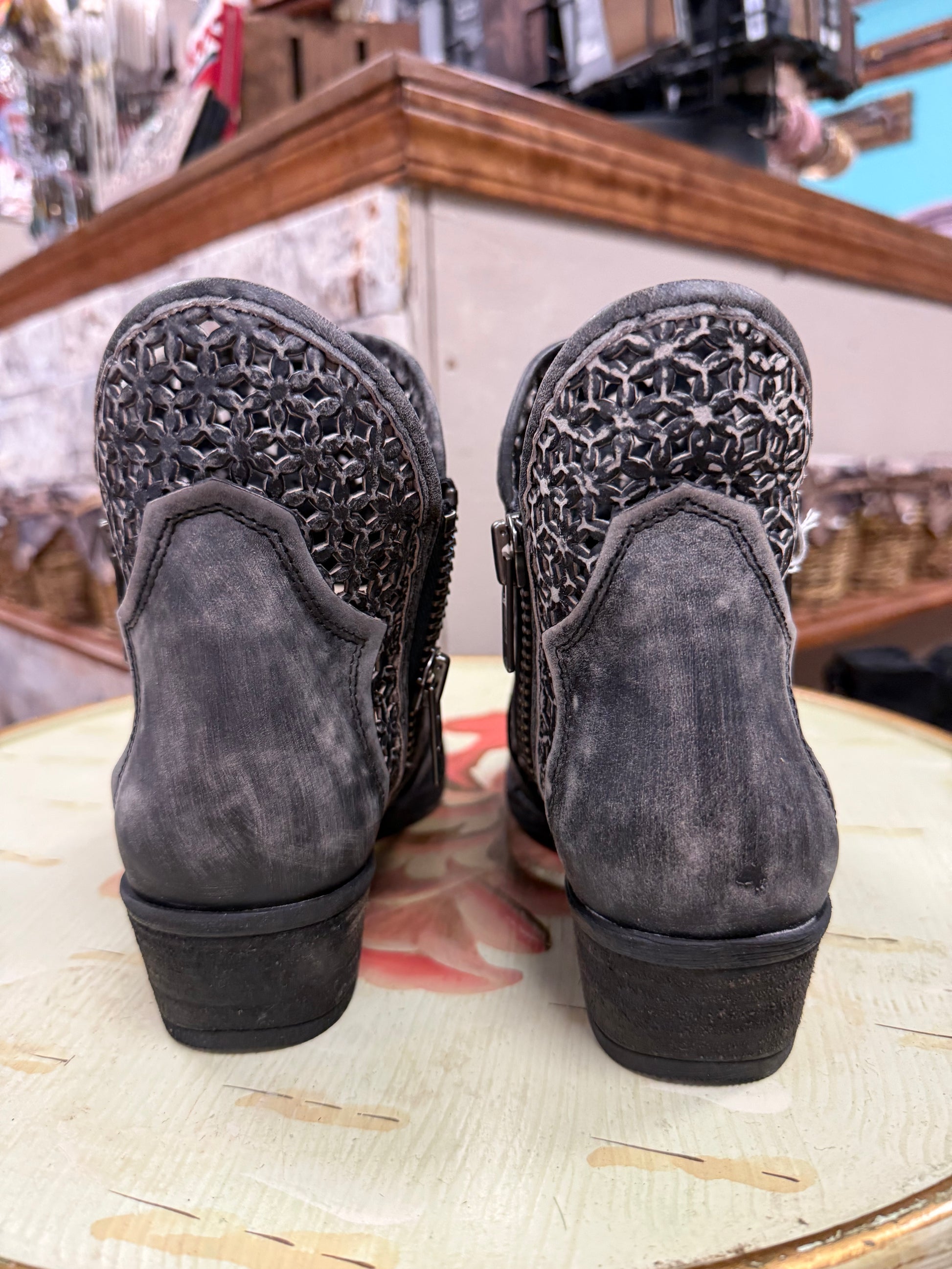 Pair of gray suede ankle boots with decorative cut-out design on a floral-patterned surface.