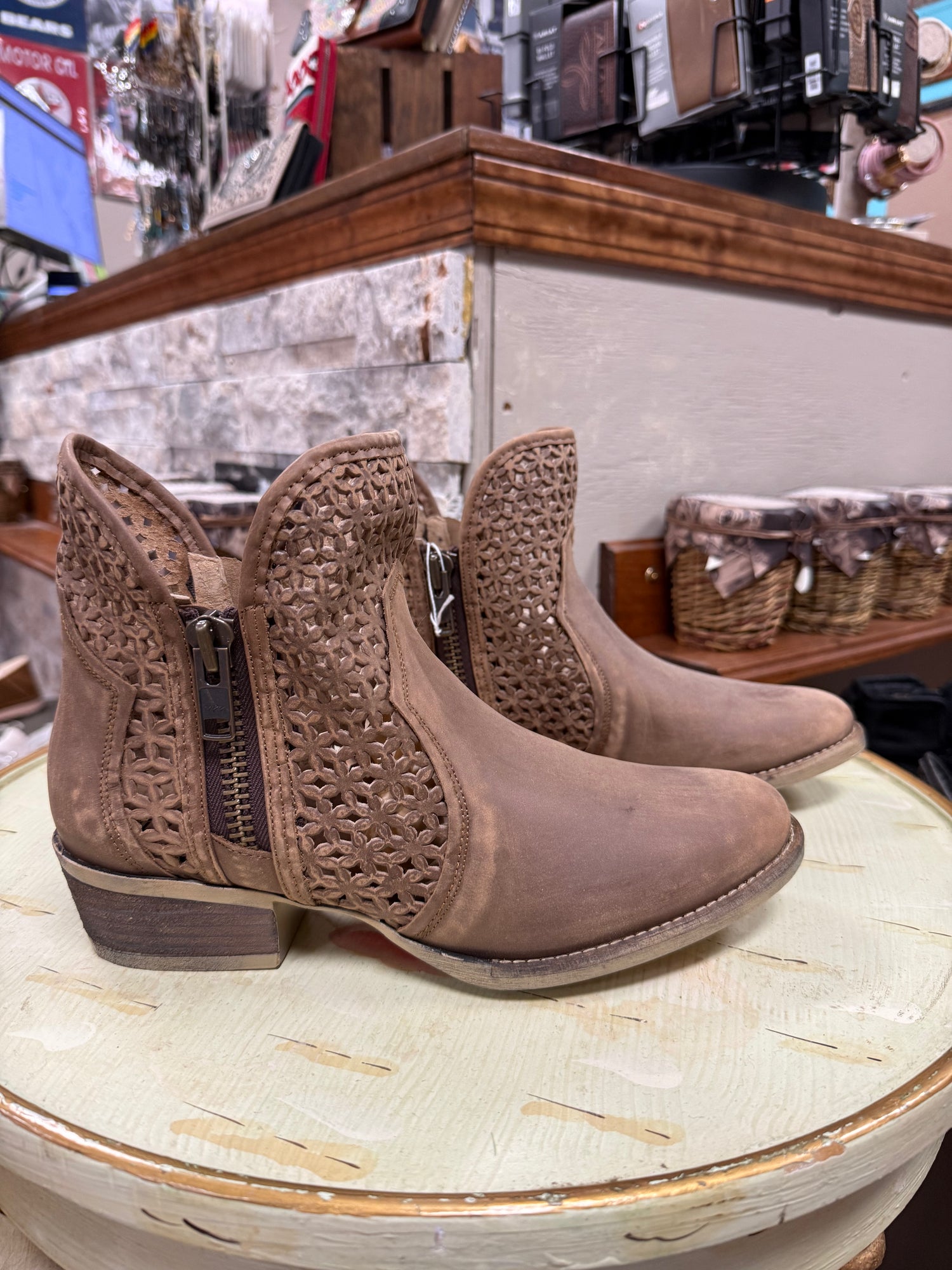 Pair of brown ankle boots with decorative cut-out design on a round surface in a store setting.
