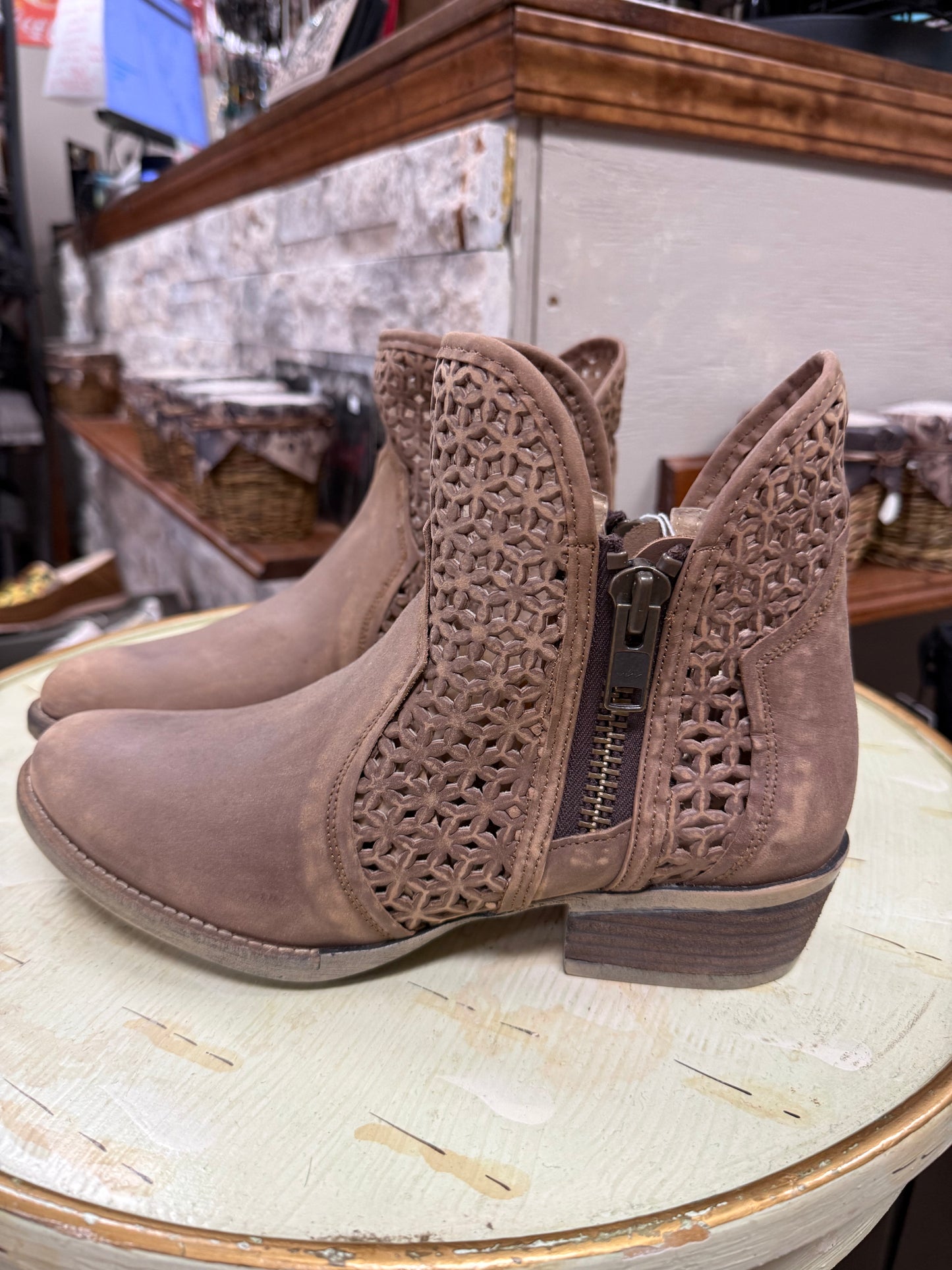 Pair of brown ankle boots with decorative cut-out design on a round table.