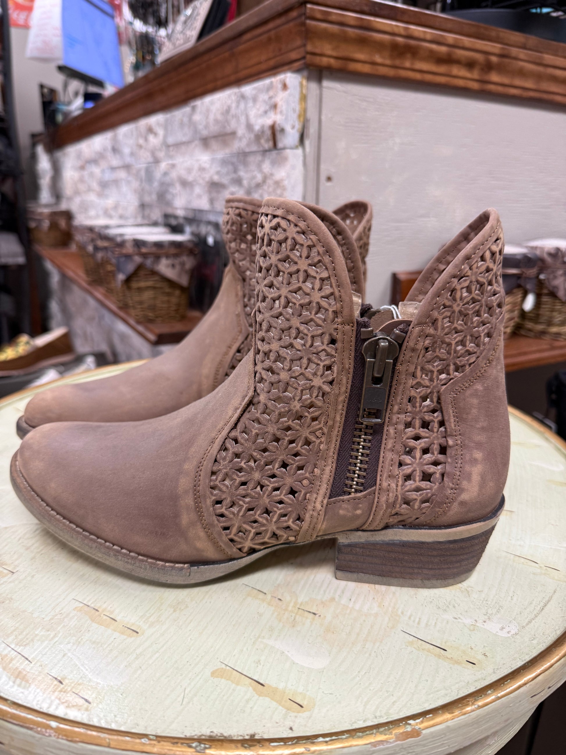 Pair of brown ankle boots with decorative cut-out design on a round table.