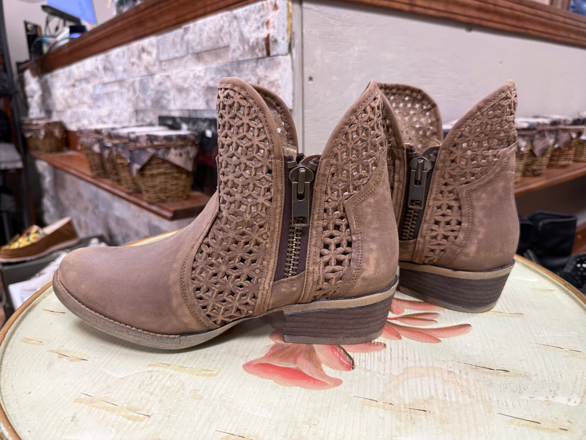 Pair of brown ankle boots with decorative patterns on a reflective surface.