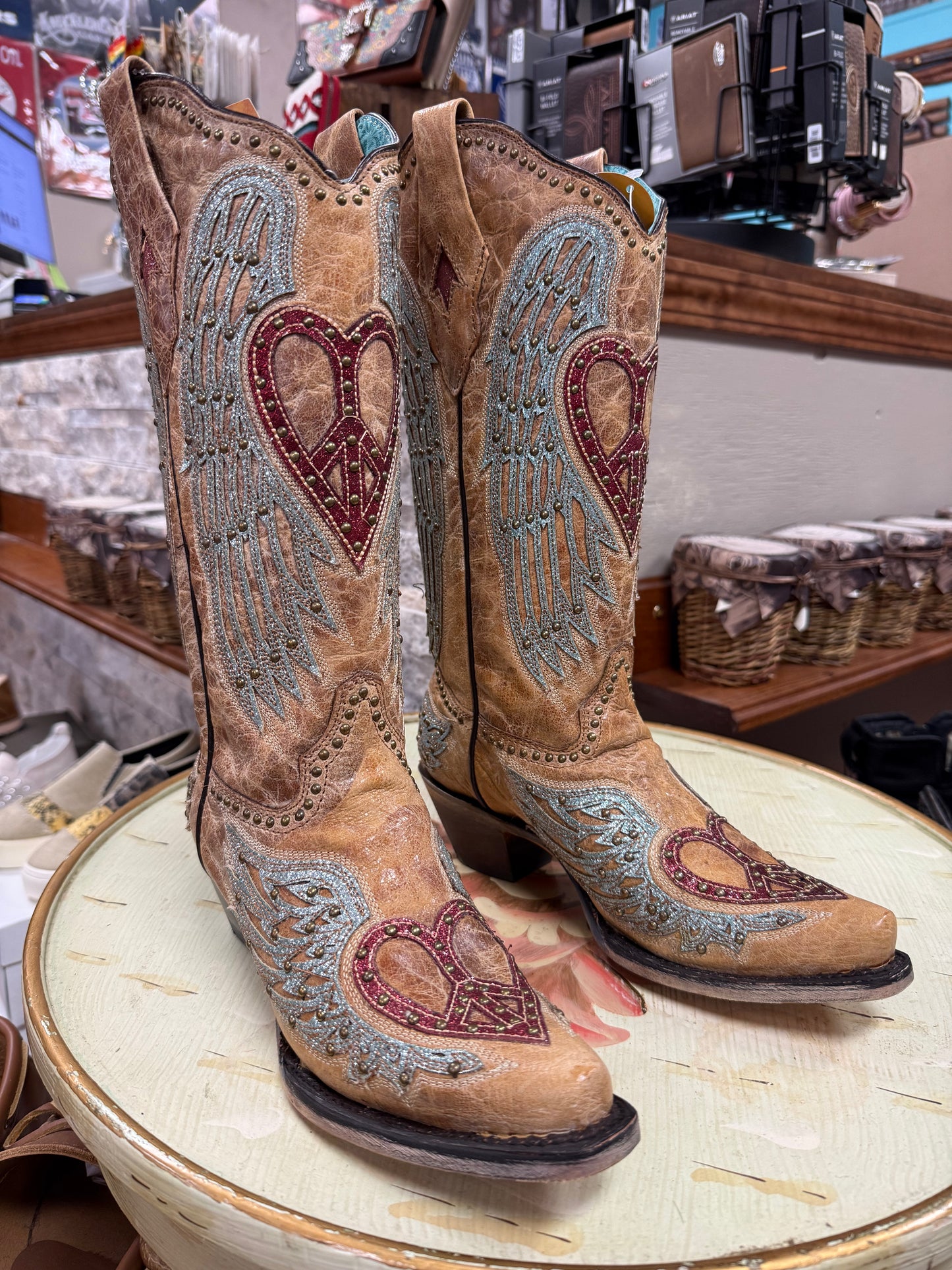 Pair of brown cowboy boots with heart and wing designs on a round surface.