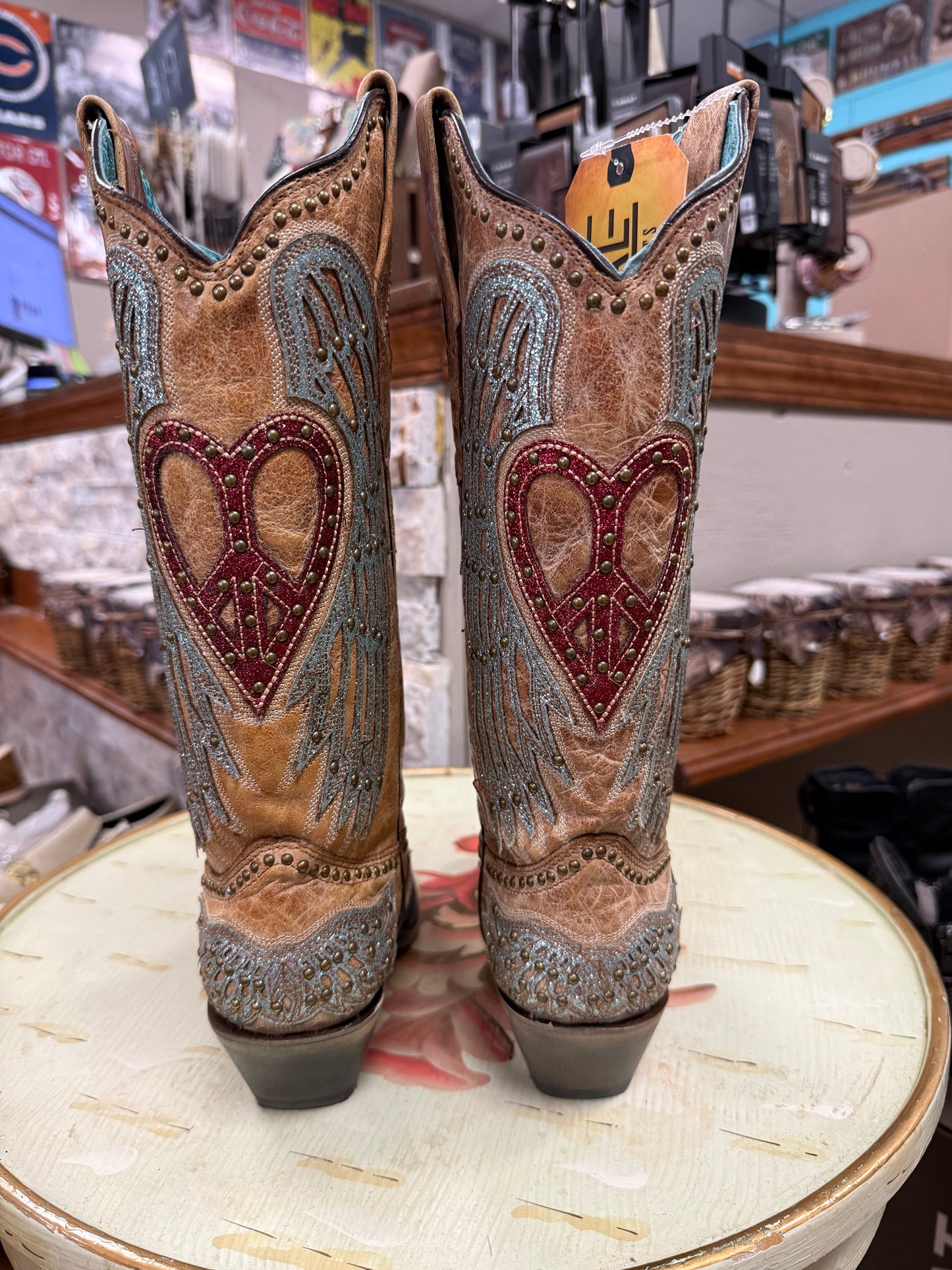 Pair of cowboy boots with heart designs on a round table in a store setting.