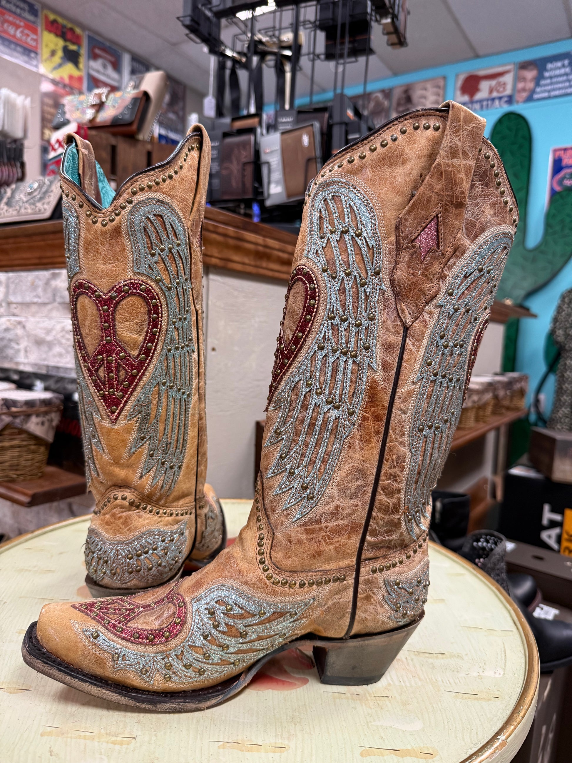 Pair of ornately decorated cowboy boots with heart and wing designs on a table.