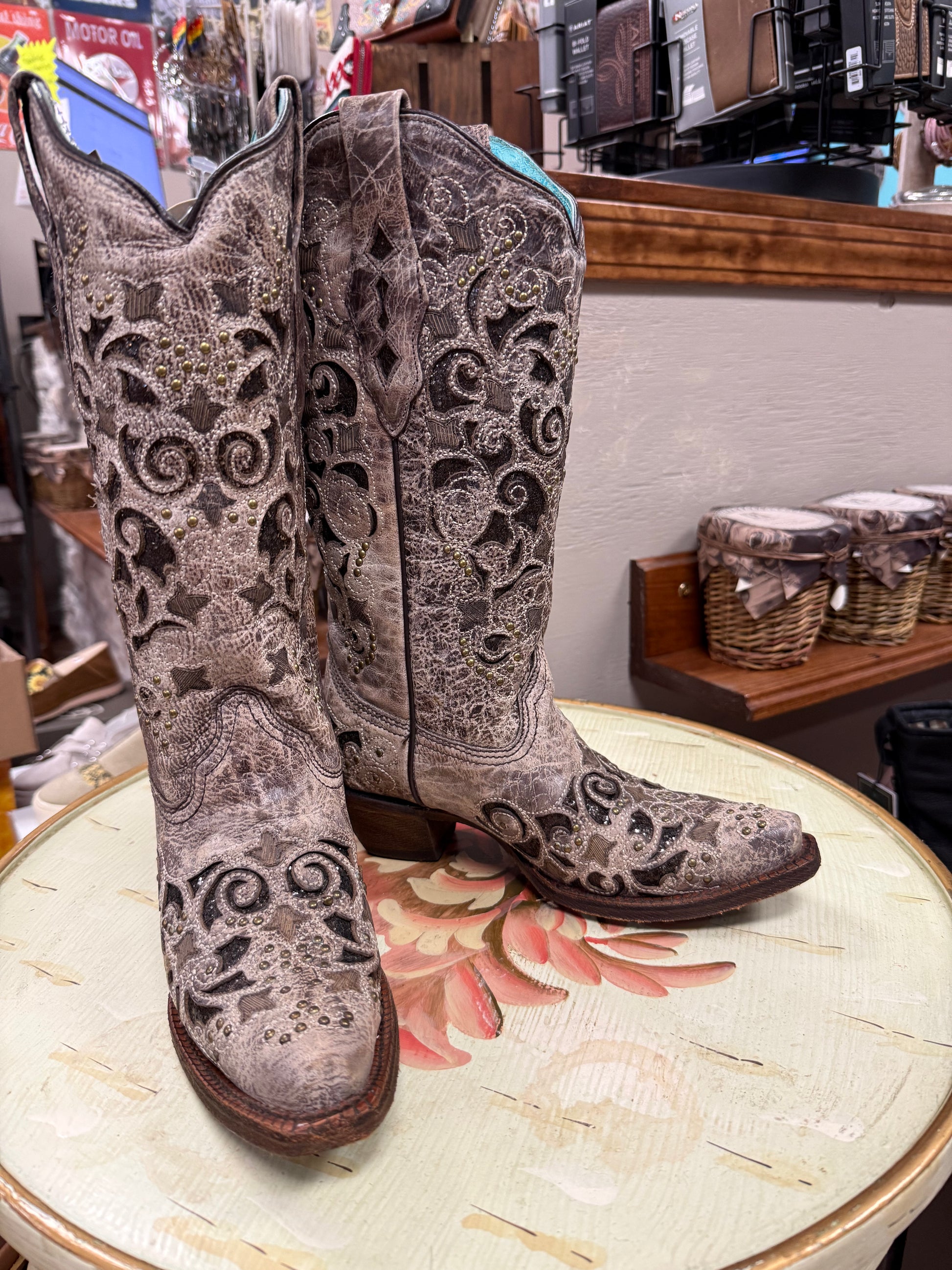 Pair of ornate cowboy boots on a floral-patterned surface with a store setting in the background.