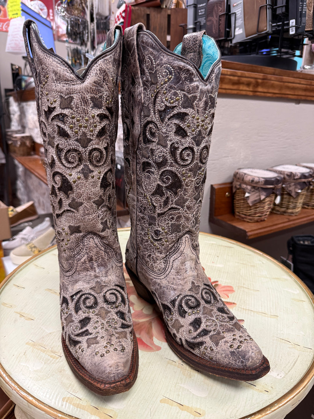 Pair of ornate cowboy boots on a round surface with a store setting in the background.