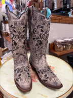 Pair of ornate cowboy boots on a round surface with a store setting in the background.