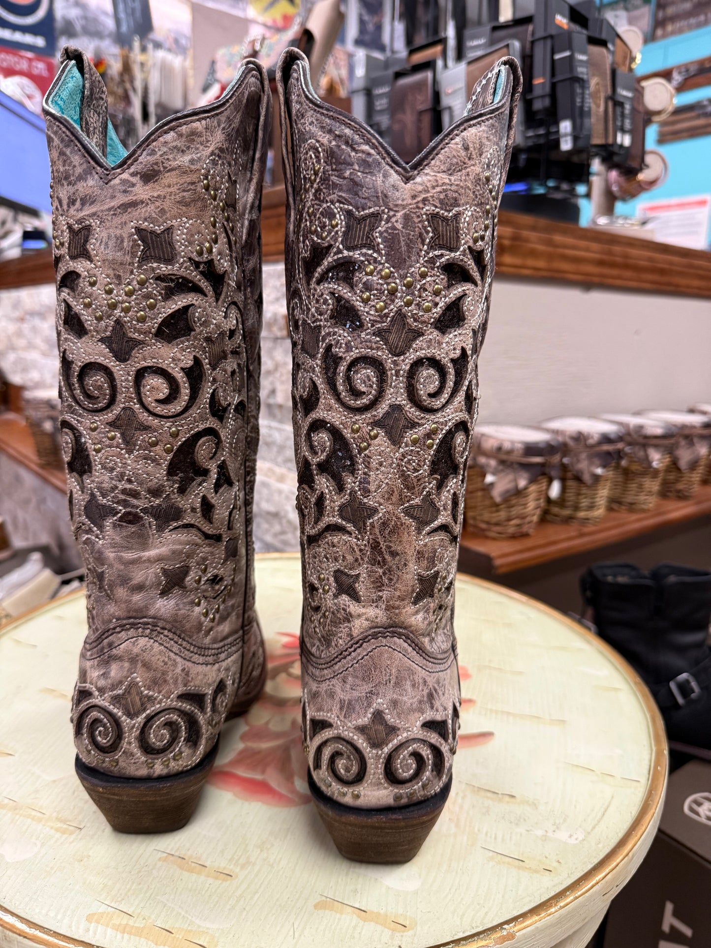 Pair of ornate cowboy boots on a round table with a store setting in the background.