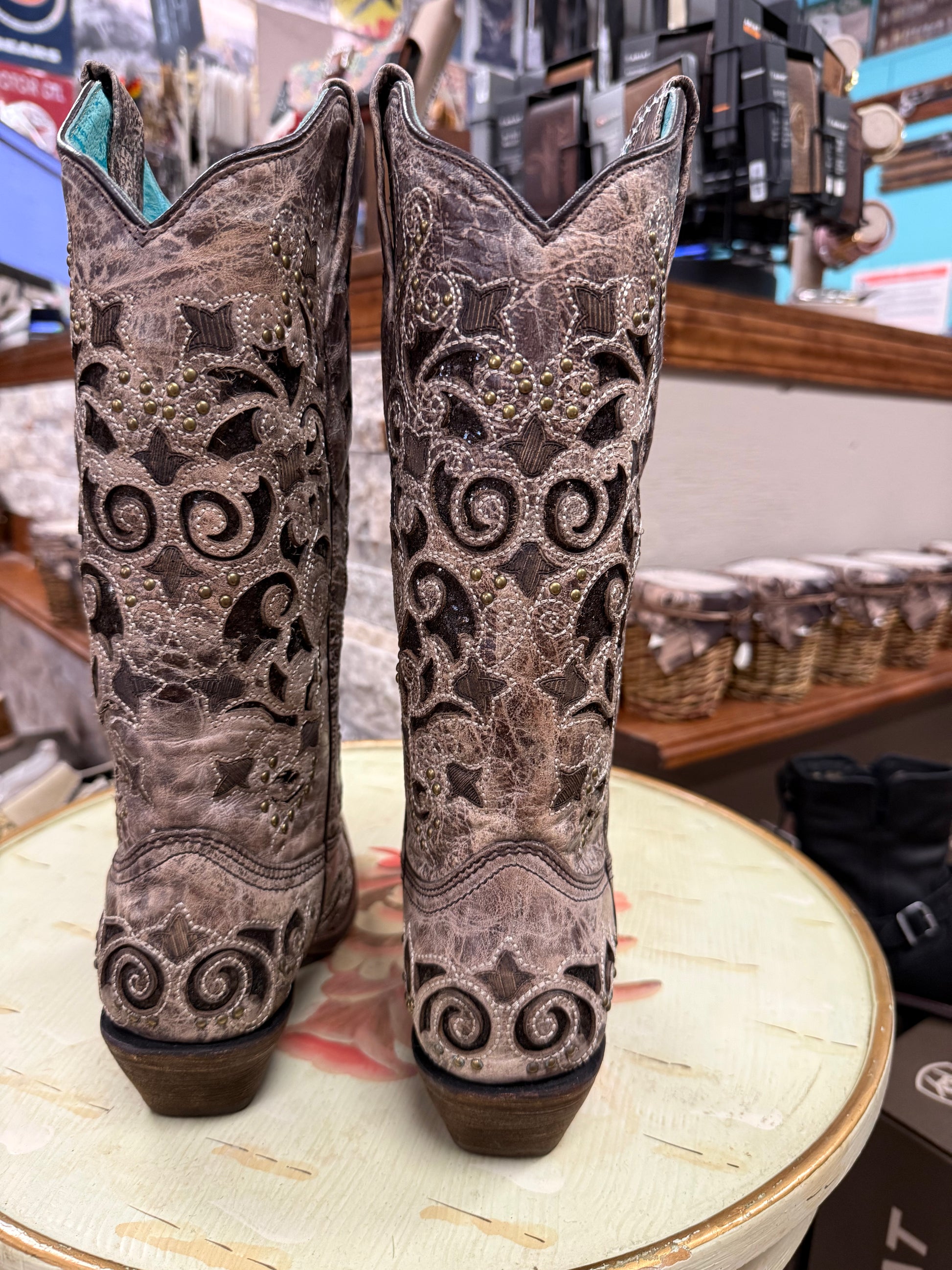Pair of ornate cowboy boots on a round table with a store setting in the background.