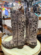 Pair of ornate cowboy boots on a round surface with a store interior background.