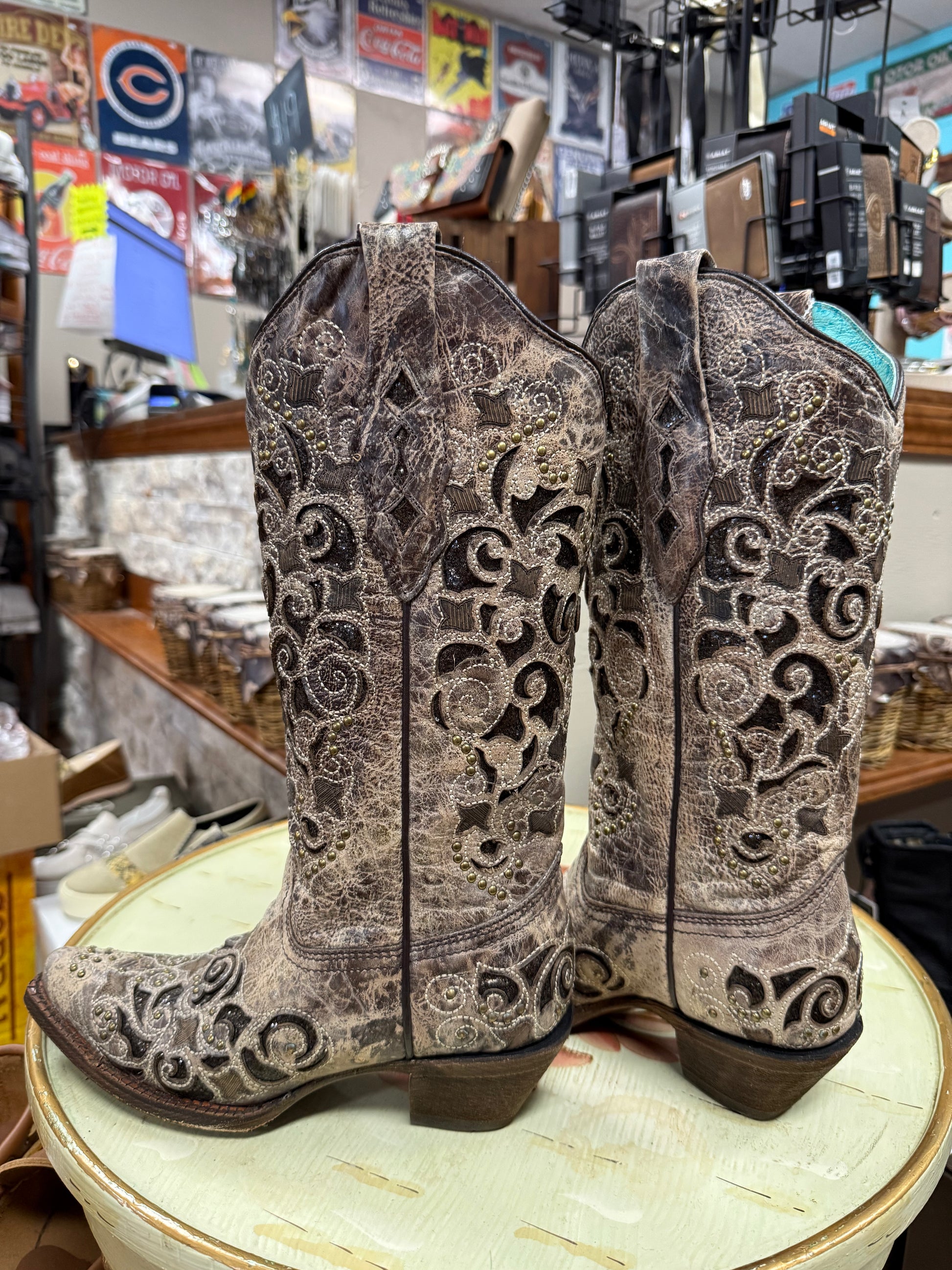 Pair of ornate cowboy boots on a round surface with a store interior background.