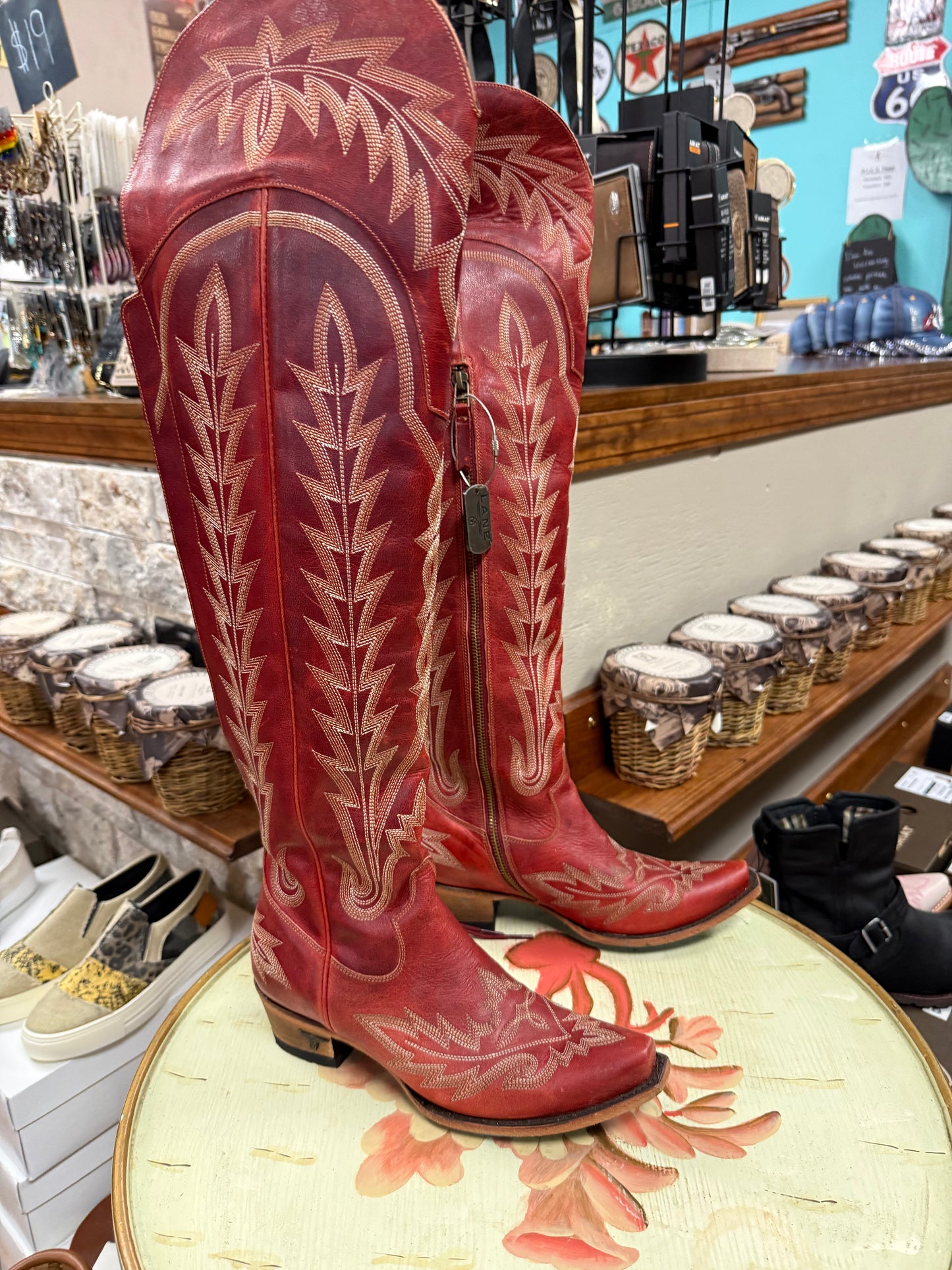 Red cowboy boots with white embroidery on a table in a store setting.
