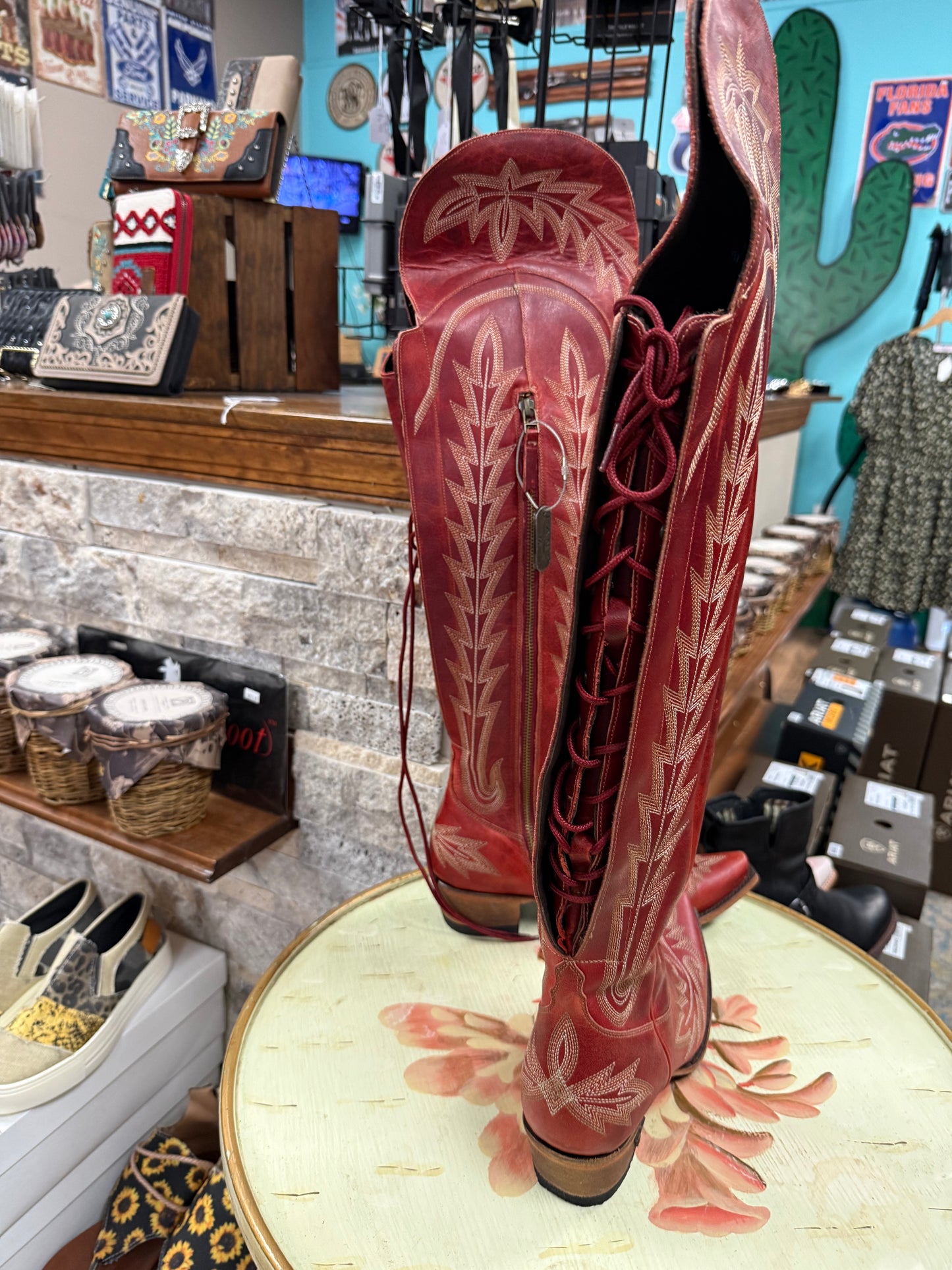 Red cowboy boots with white patterns on a floral table in a store setting.