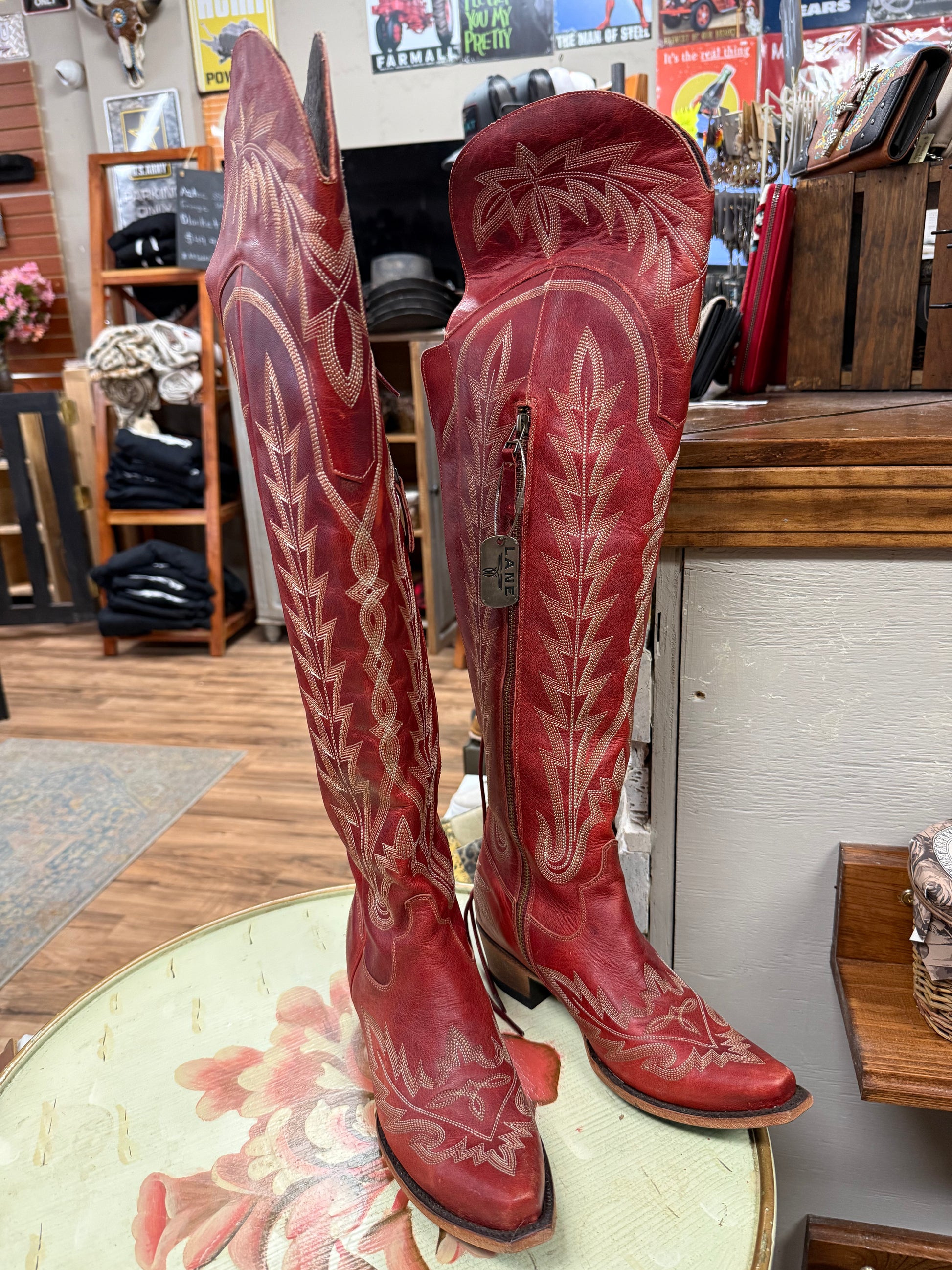 Red cowboy boots with white embroidery on a floral table in a store setting.