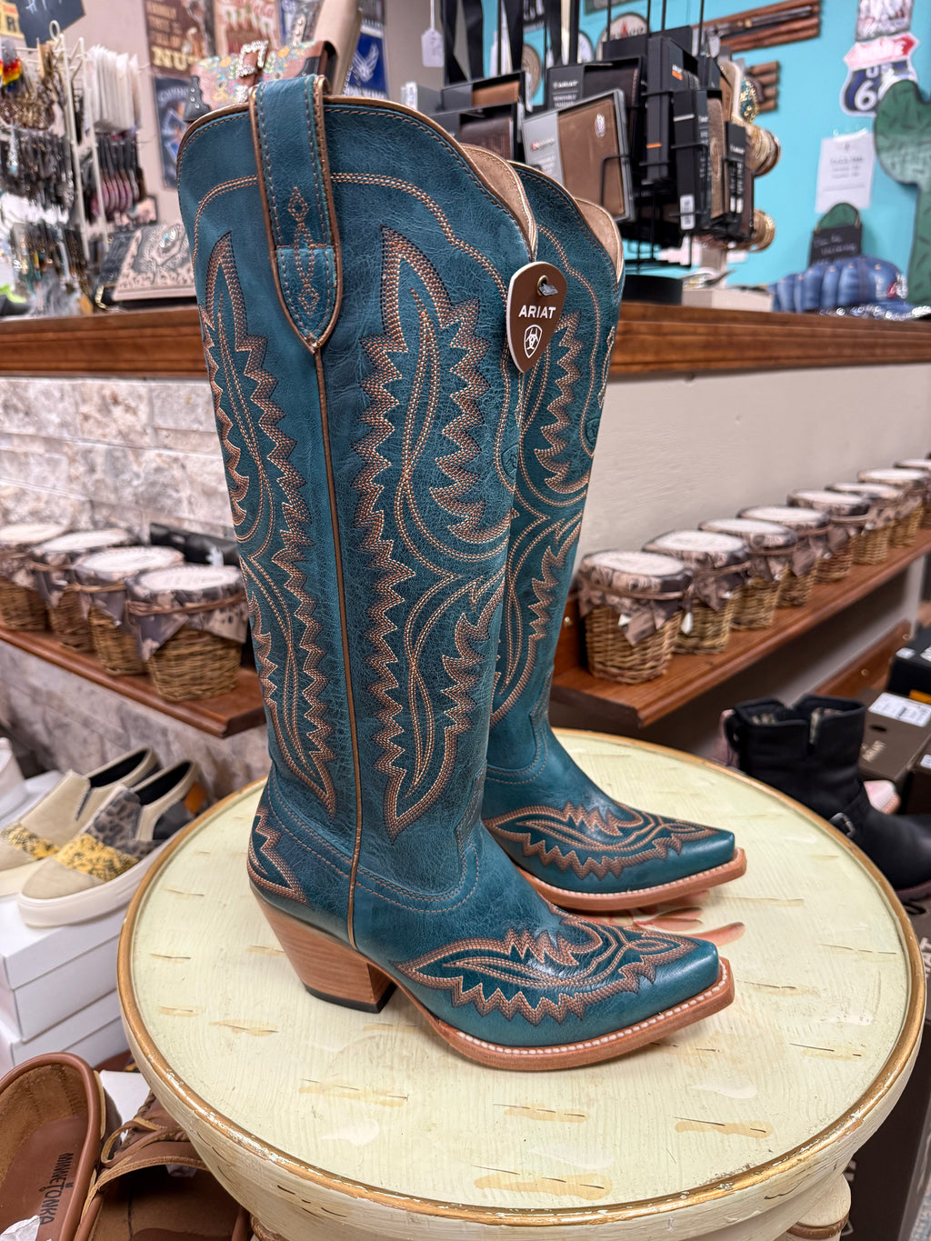 Blue cowboy boots with intricate designs on a round table in a store setting.