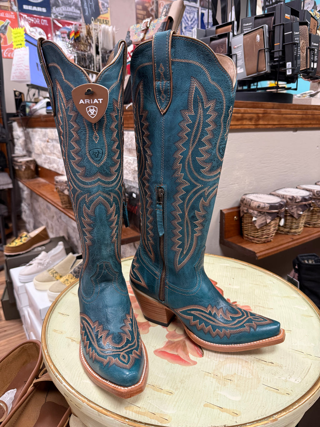 Pair of blue Ariat cowboy boots on a round table in a store setting.