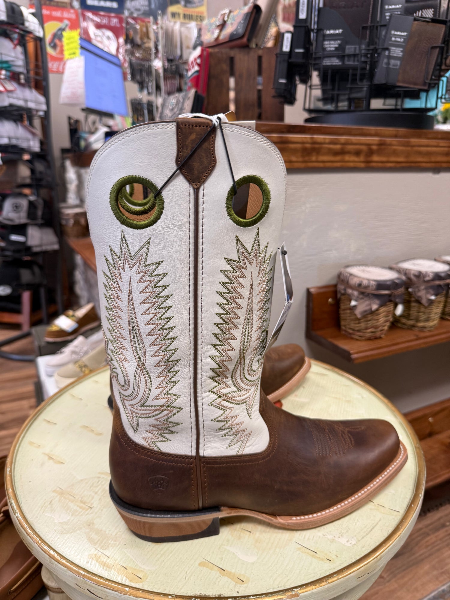 Brown and white cowboy boot with intricate embroidery on a round stool in a store setting.