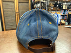 Blue denim cap with yellow stitching on a wooden surface in a store setting