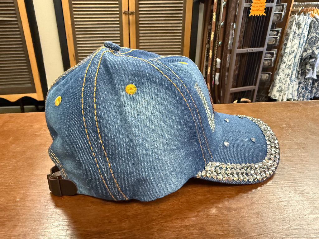 Blue denim cap with yellow buttons and rhinestone embellishments on a wooden surface.
