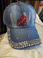 Blue denim cap with rhinestone embellishments and a red heart design on a beige surface.