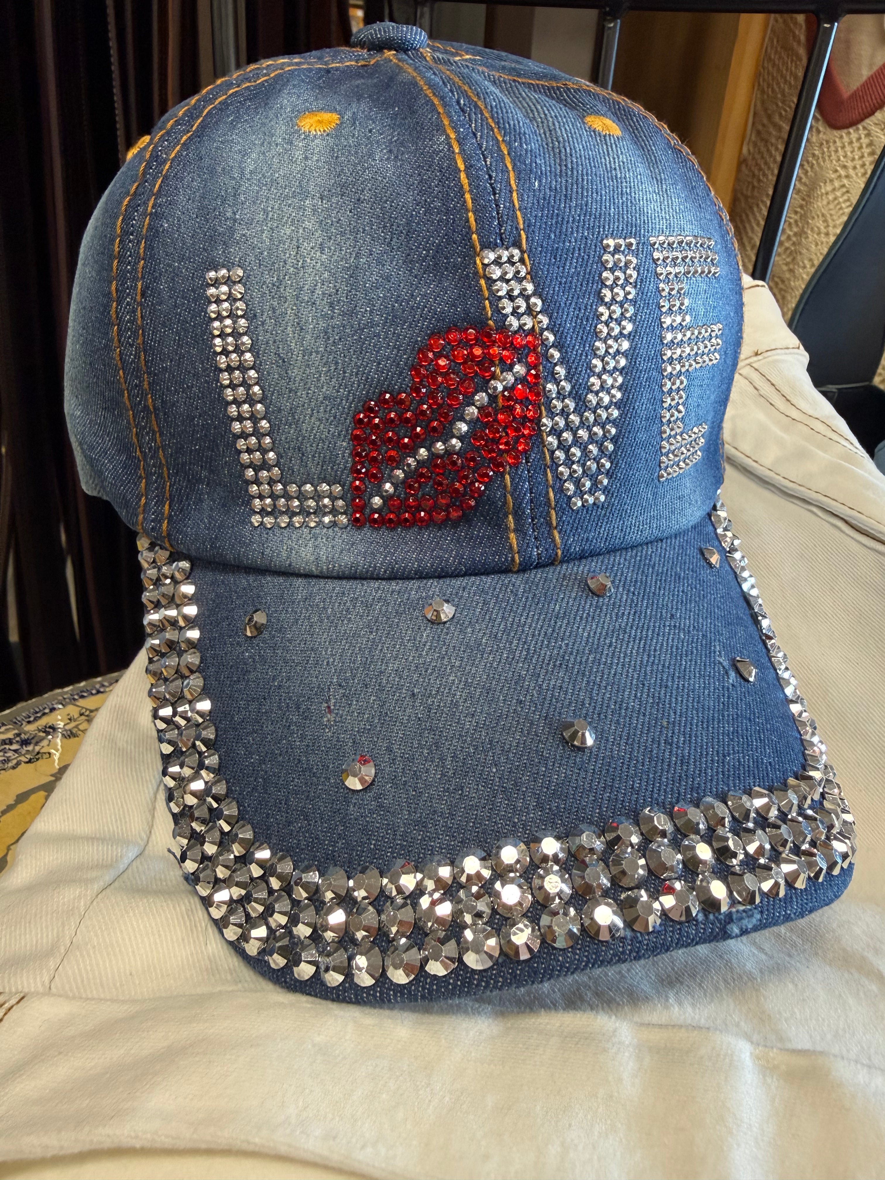 Blue denim cap with rhinestone embellishments and a red heart design on a beige surface.