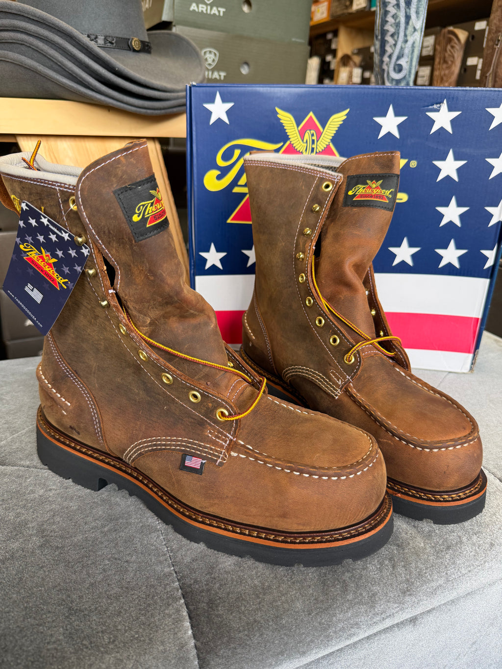 Pair of brown work boots with Ariat logo in front of an American flag box.