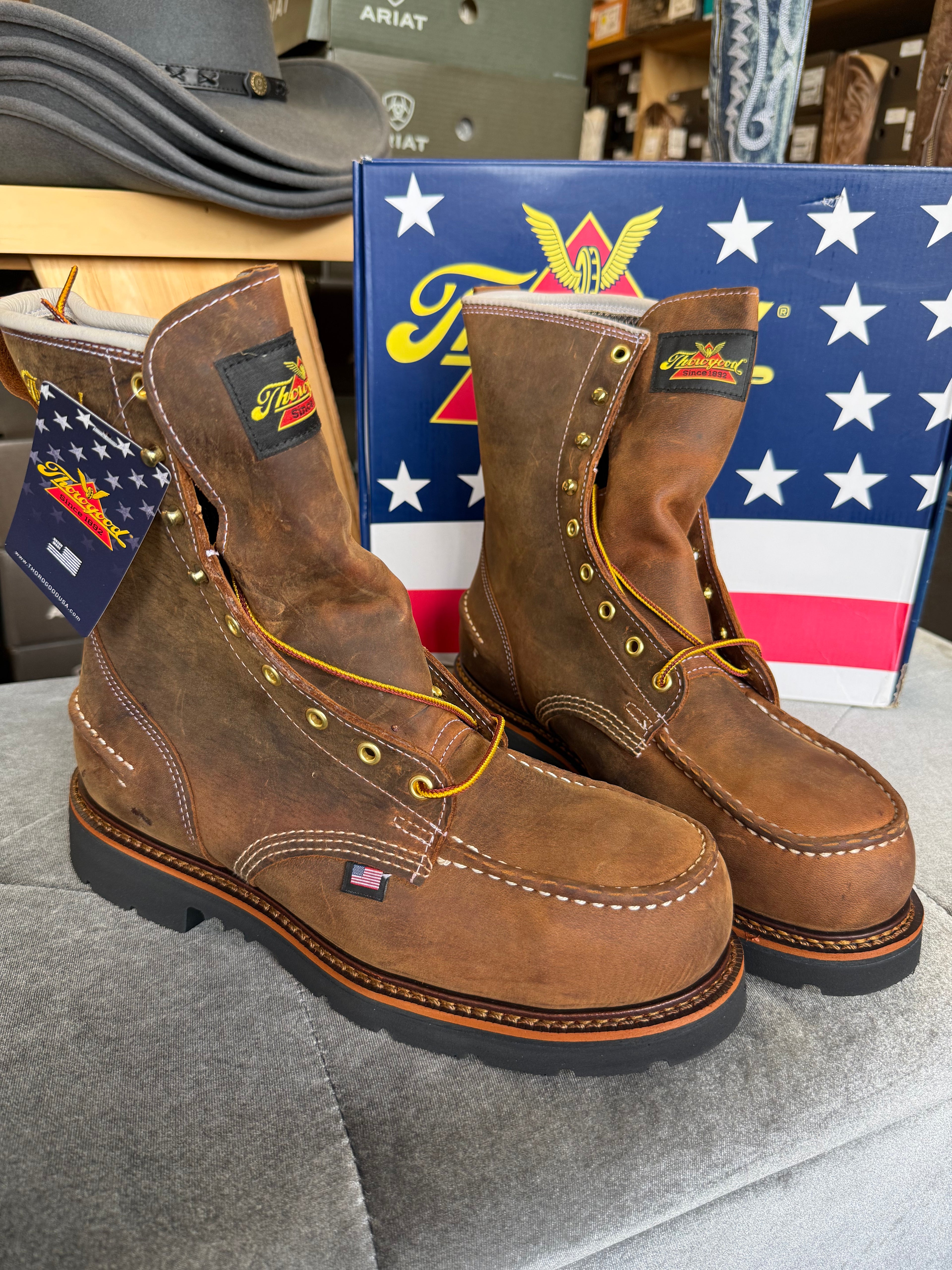 Pair of brown work boots with Ariat logo in front of an American flag box.