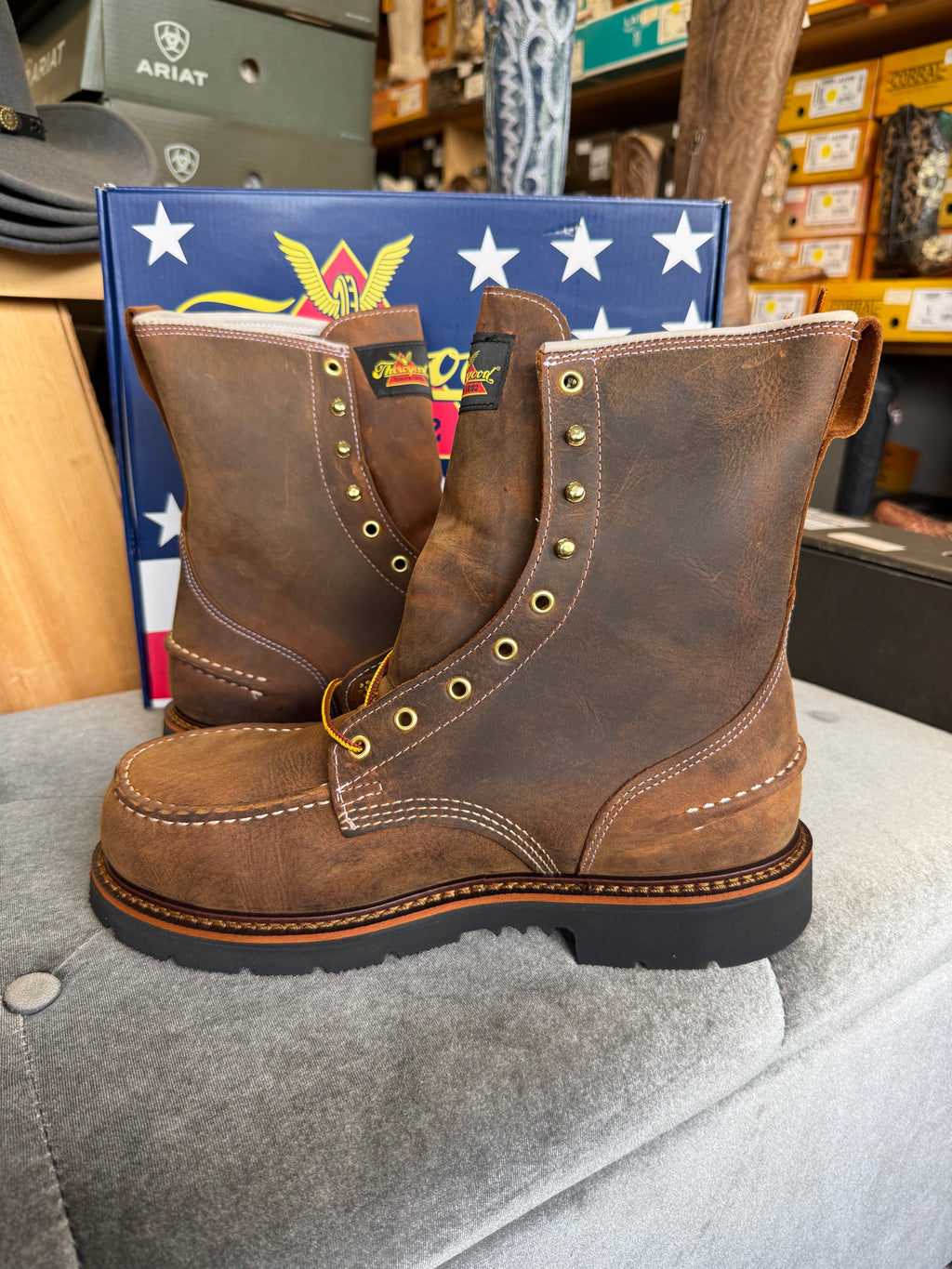 Brown leather boots with gold buttons on a gray surface, with a colorful box in the background.