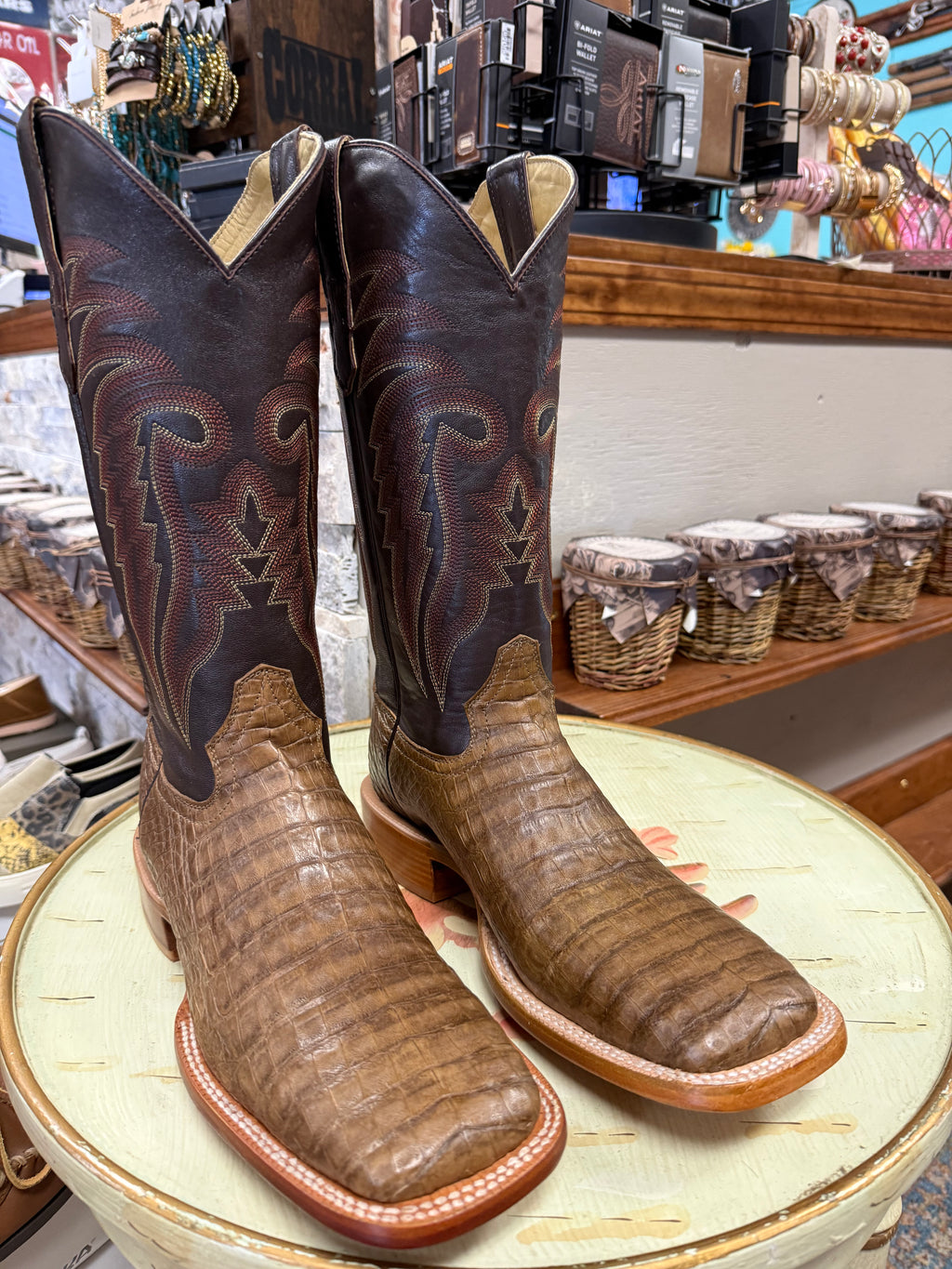 Pair of brown cowboy boots with intricate designs on a round surface in a store setting.