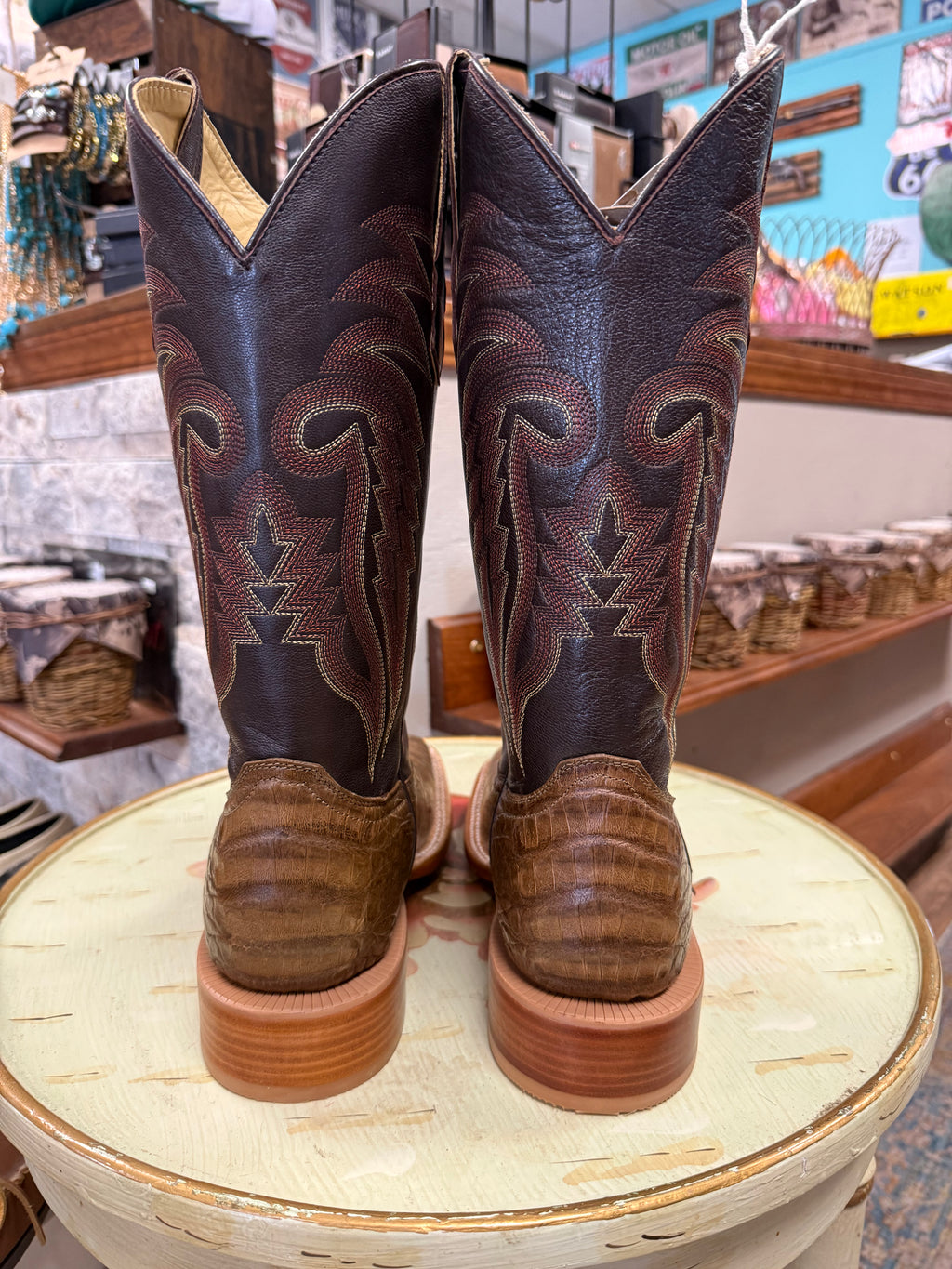 Pair of brown cowboy boots with intricate patterns on a round wooden stool in a store setting.
