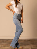 Person wearing a white t-shirt and blue flared jeans on a plain background