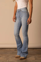 Person wearing light blue jeans on a wooden floor with a beige wall background