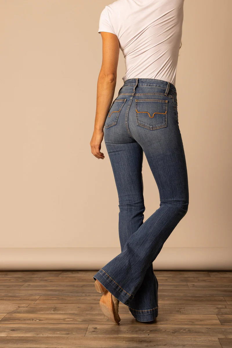Person wearing blue jeans and a white top on a wooden floor with a beige wall background