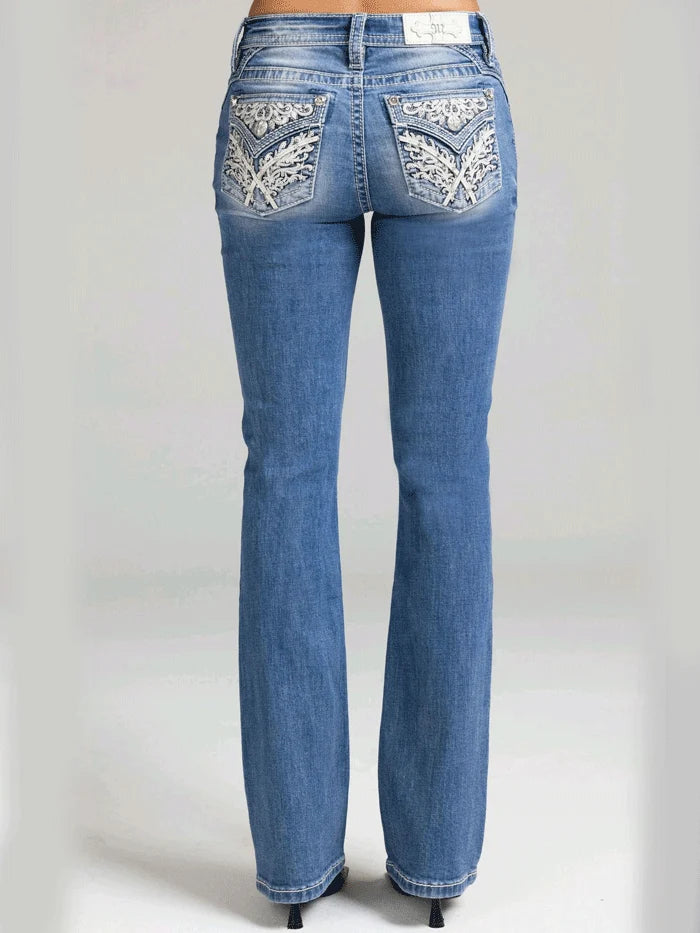 Rear view of a person wearing blue denim jeans with ornate white embroidered detailing on the back pockets, shown against a light gray studio background.
