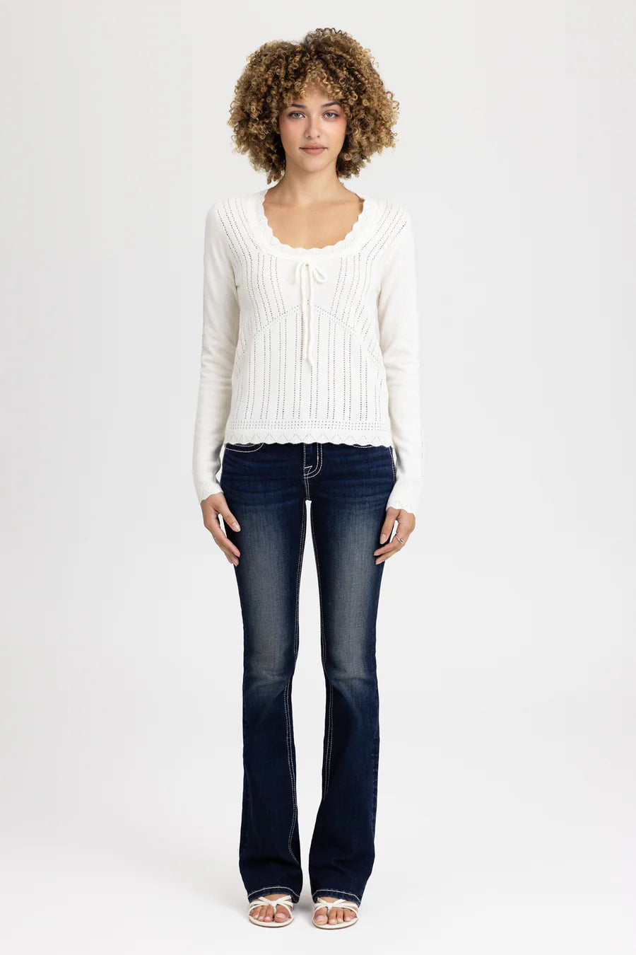 Woman wearing a white sweater and dark jeans on a white background