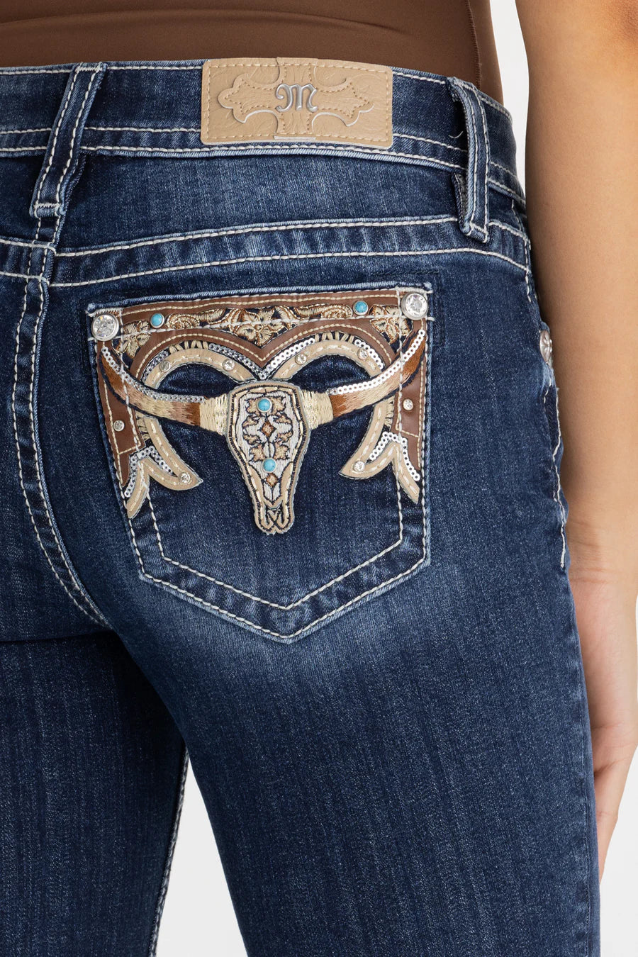 Close-up of blue jeans with decorative back pocket featuring a bull head design.