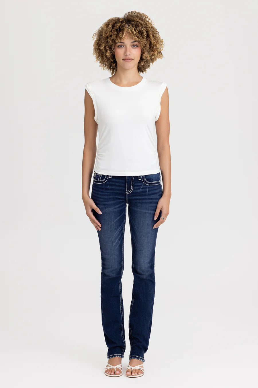 Woman wearing a white sleeveless top and blue jeans on a white background