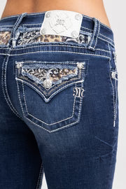 Close-up of blue jeans with decorative stitching and a brand logo on a white background