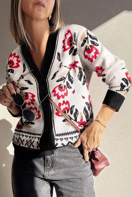 Woman wearing a floral patterned cardigan with sunglasses and a pink clutch against a neutral background