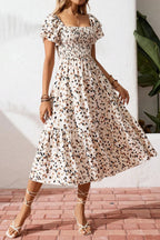 Woman wearing a floral dress standing against a white wall with a plant in the background.