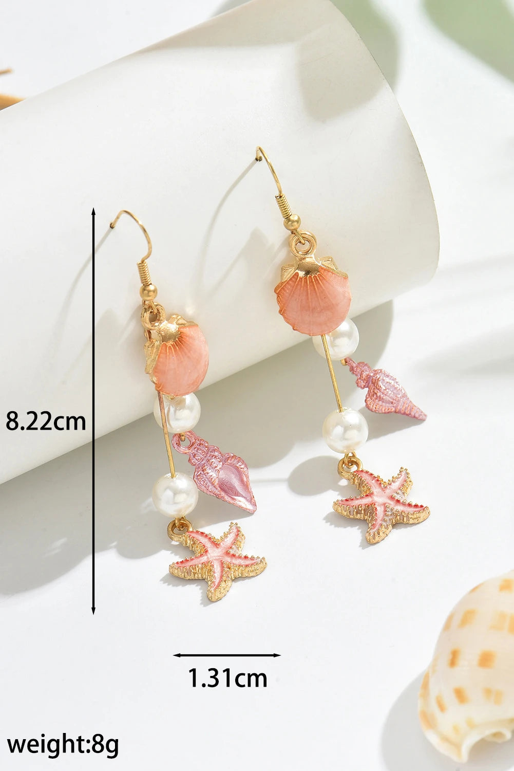 Pair of earrings with starfish and shell designs on a white surface.