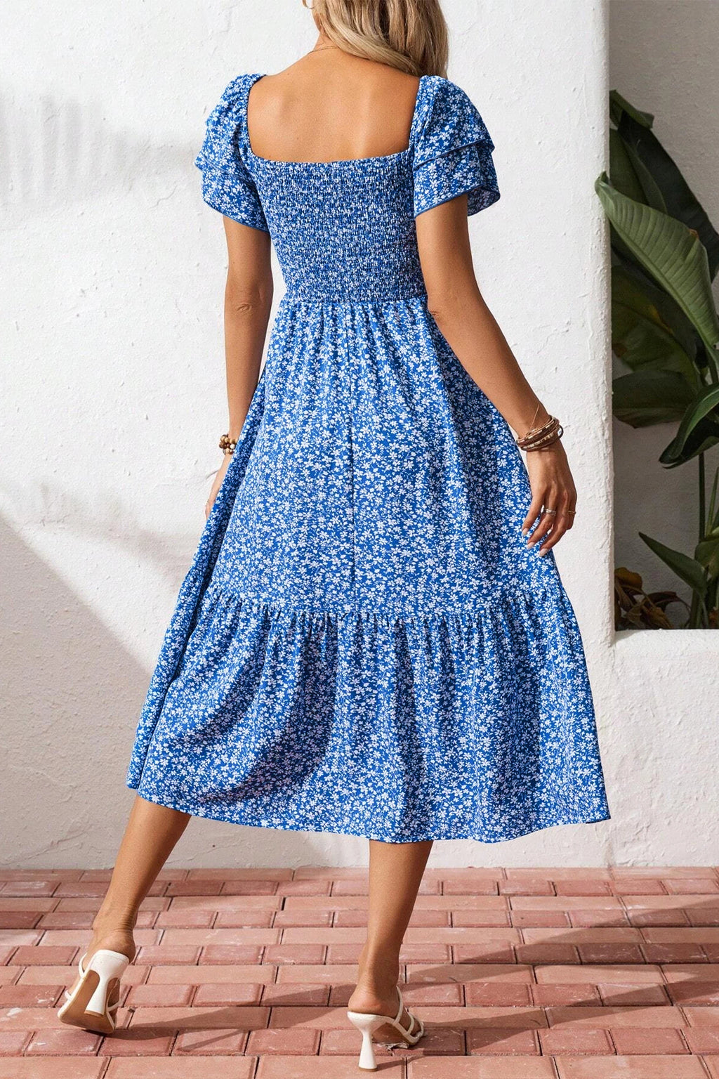 Woman wearing a blue floral dress with a white wall and plant in the background