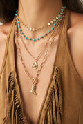 Necklace with turquoise beads and gold chain on a person wearing a brown top.