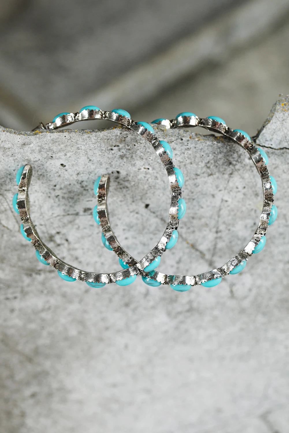 Silver hoop earrings with turquoise accents on a stone surface