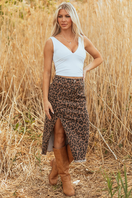 Woman in a leopard print skirt and white top standing in a field of tall dry grass.