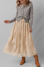 Woman wearing a gray shirt and beige lace skirt with brown boots on a plain background